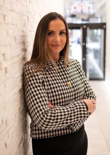 Kendra McKinney, legal professional at Astraea Linskills Solicitors Liverpool, standing with arms crossed against a textured wall.