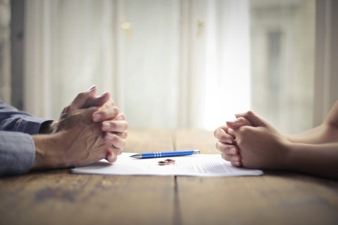 Two individuals with clasped hands on a table during a tense divorce negotiation, highlighting the need for legal support from Astraea Linskills Solicitors Liverpool.