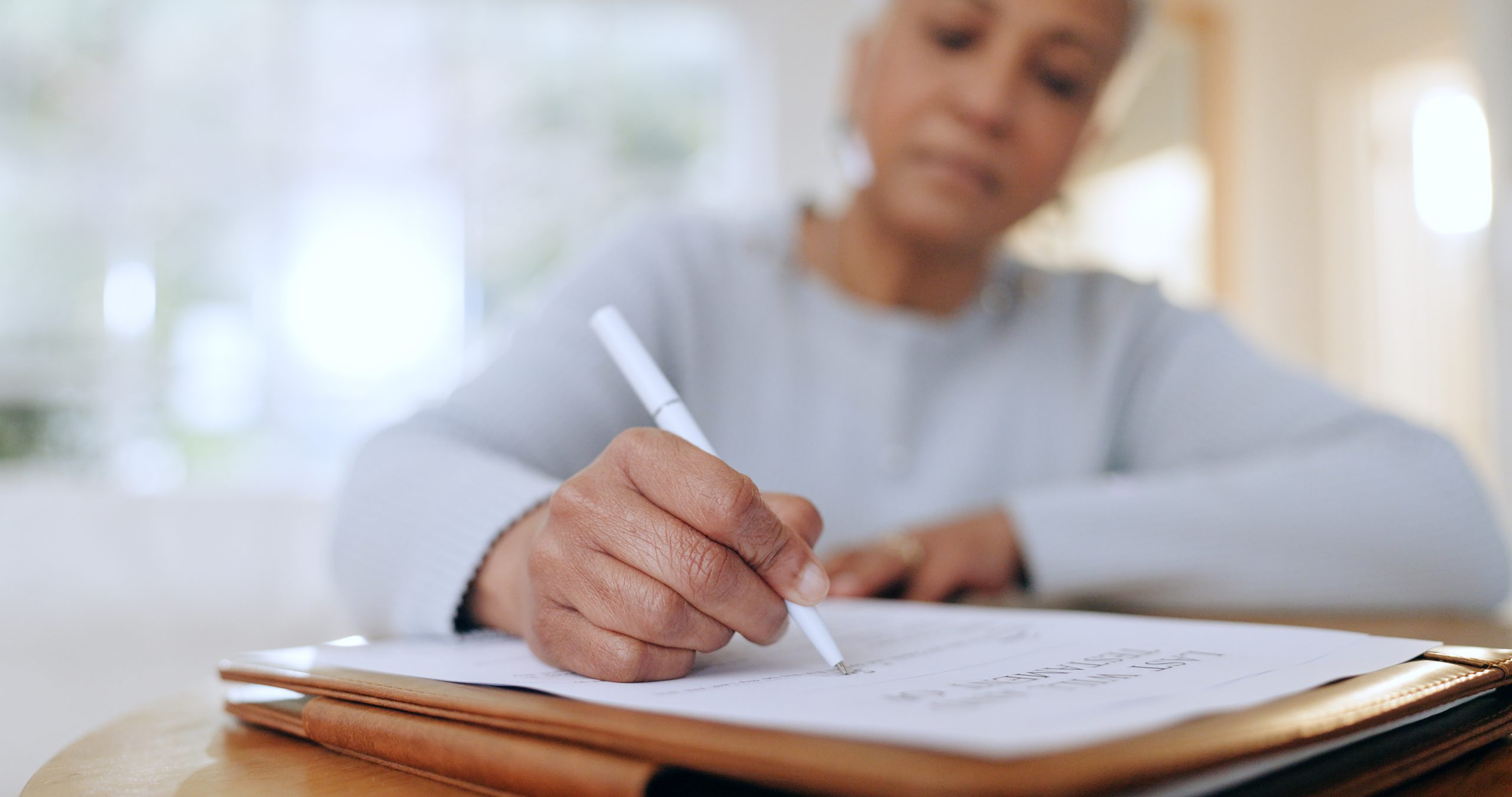 Senior woman signing legal documents, symbolizing the process of will creation and estate planning with assistance from Astraea Linskills Solicitors Liverpool.