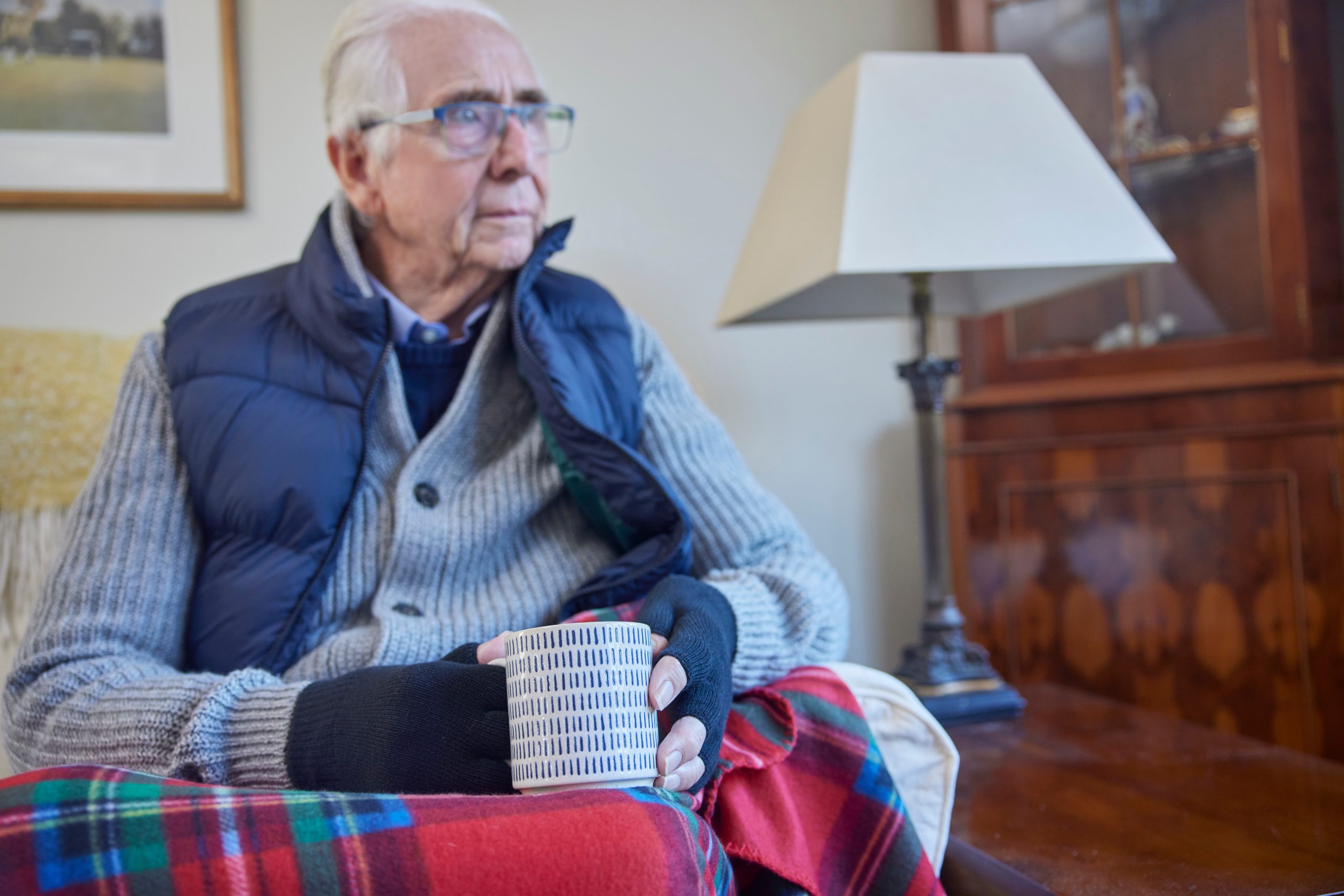 An elderly man wrapped in a blanket holding a mug, highlighting the cost of living crisis and housing disrepair issues, assisted by Astraea Linskills Solicitors Liverpool.