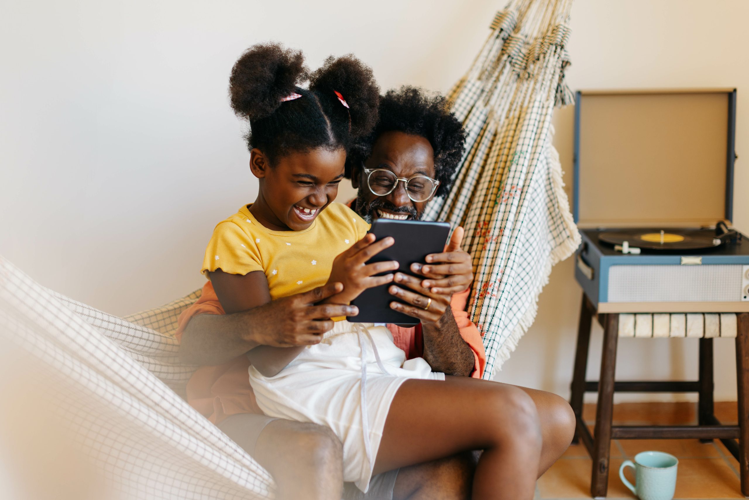 Dad and daughter relaxing together in hammock, laughing and watching a video on a tablet cohabitation agreement